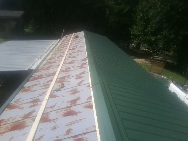 Old rusted panels beside newly installed green metal roofing — Wind Damage Roof Repair by Roofing Brothers in Brightwood