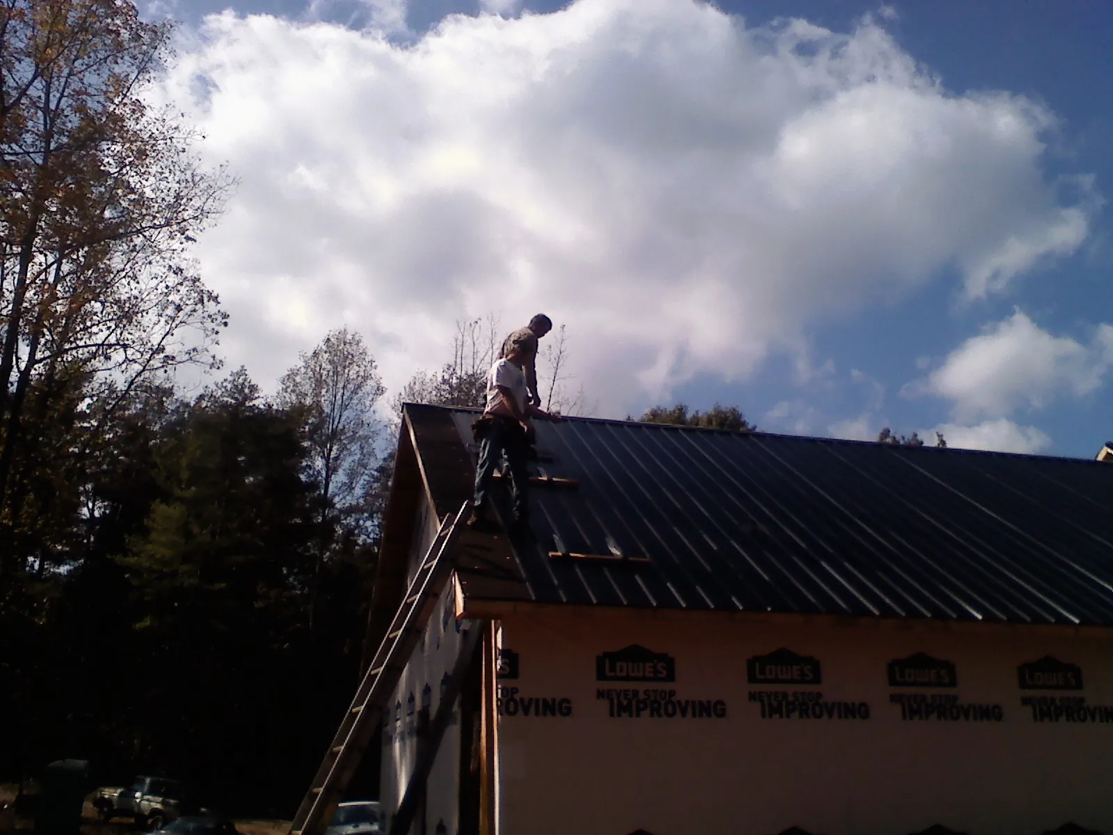 Roofer fastening dark metal panels high against a cloudy sky, from a Roof Inspection job in Brightwood