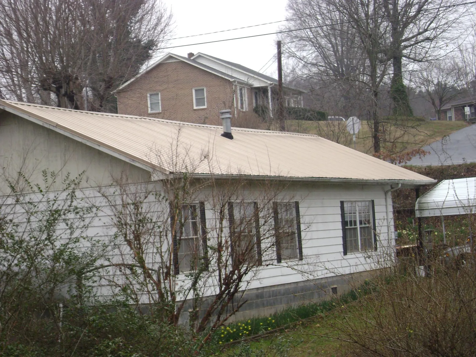 Tan metal roof on a white sided house set into a hillside — Commercial Roofing by Roofing Brothers in Brightwood